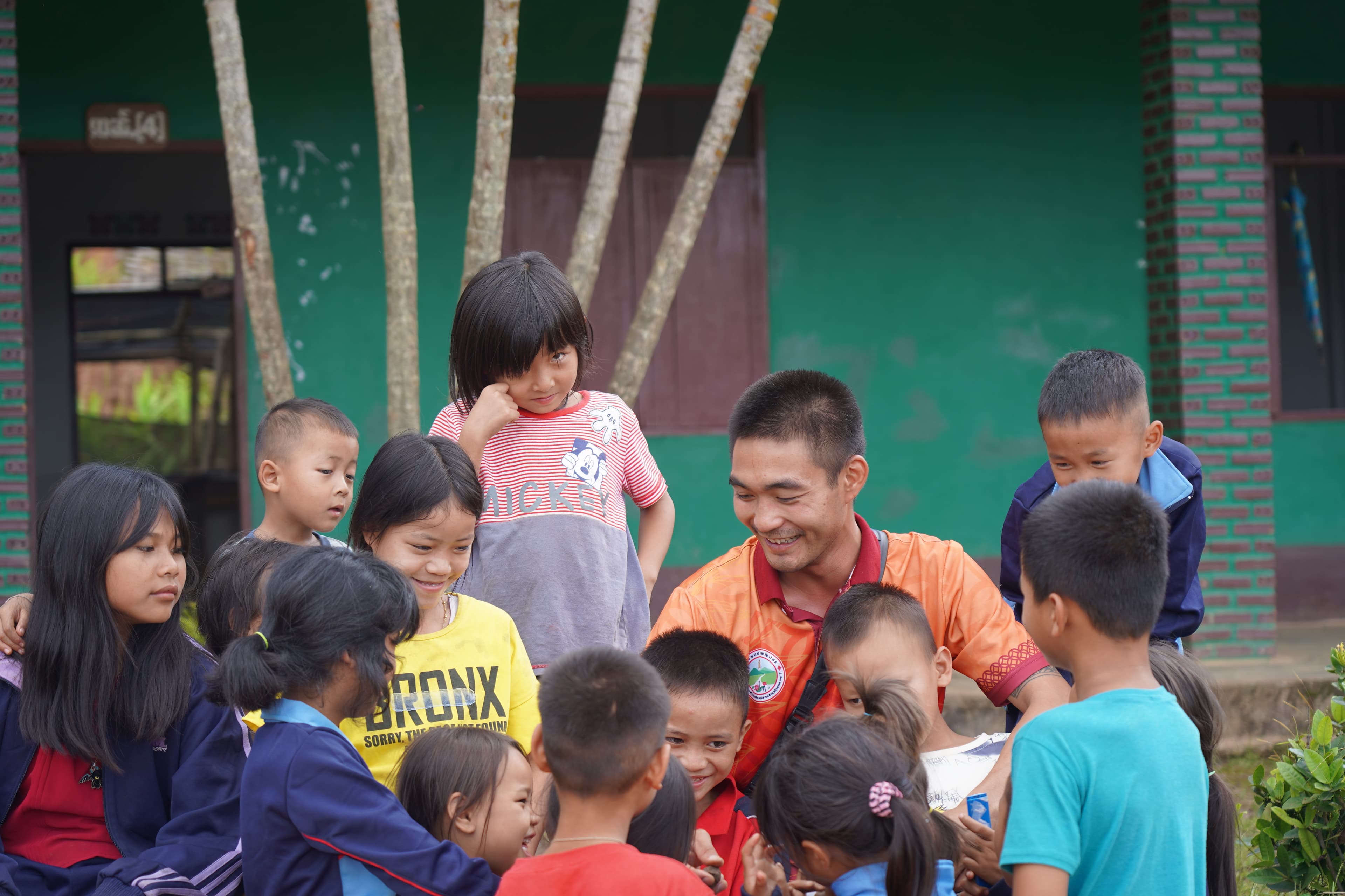 An ESSENCE team member sitting with a group of village children outside their school